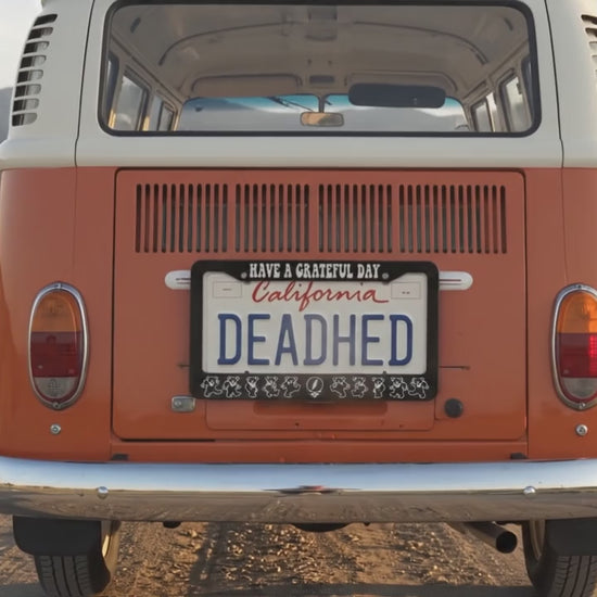 Orange retro hippie van on gravel road driving through grassy hills