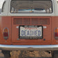Orange retro hippie van on gravel road driving through grassy hills